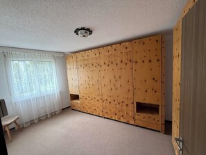 A room with a large wooden wardrobe, a small wooden table, and a window with sheer curtains. - Parsennresidenz 403 Appartement/Fewo, Dusche oder Bad, WC 2½-Zimmerwohnung by Interhome (Davos)