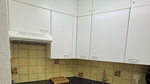Ett kompakt kök med vita skåp, en svart bänkskiva, en spis, ett diskho och en diskmaskin.