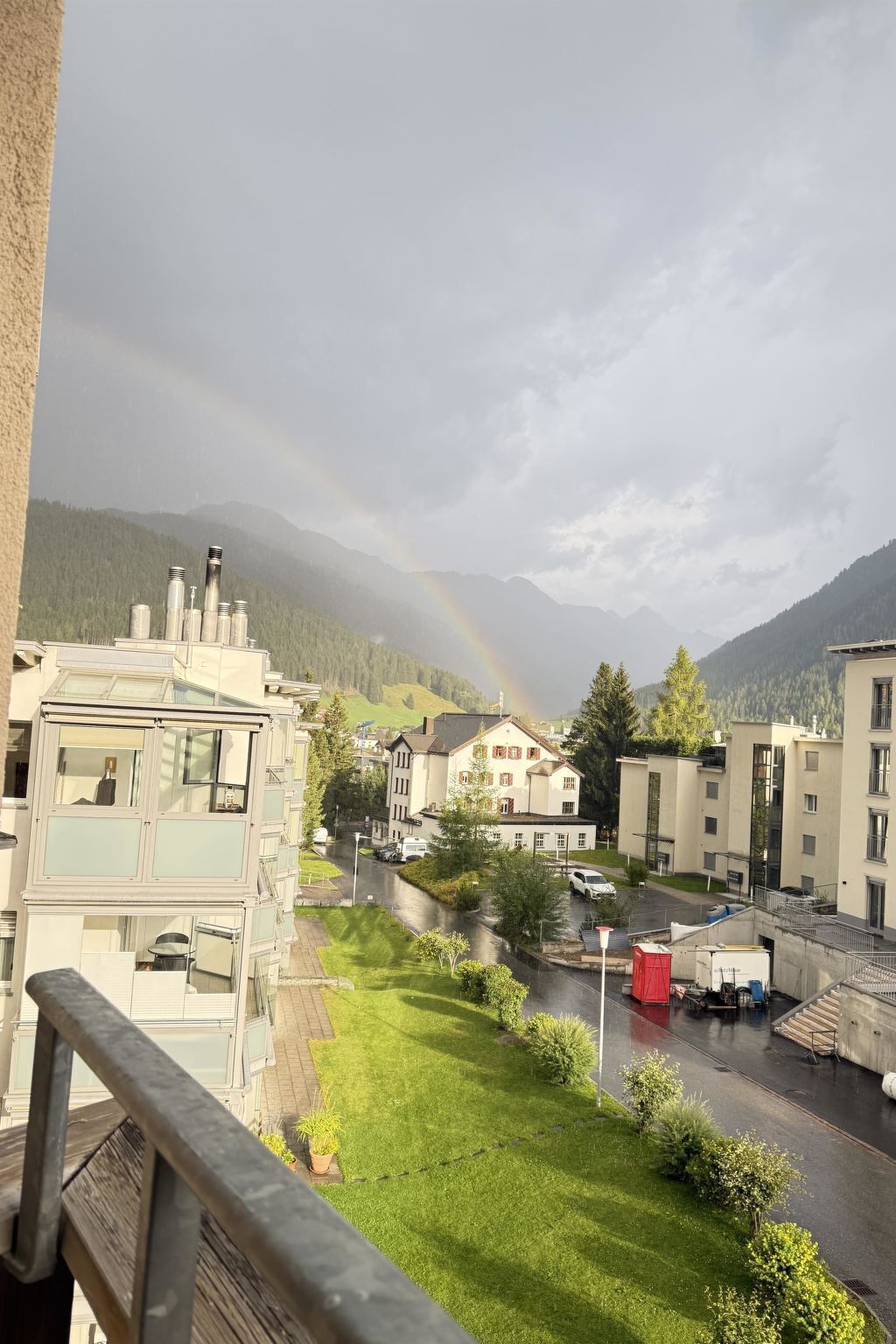 A residential area with buildings, a green lawn, and a mountain range in the background.