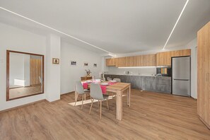A modern kitchen with wooden cabinets, a dining area with a table set for two, and a refrigerator.