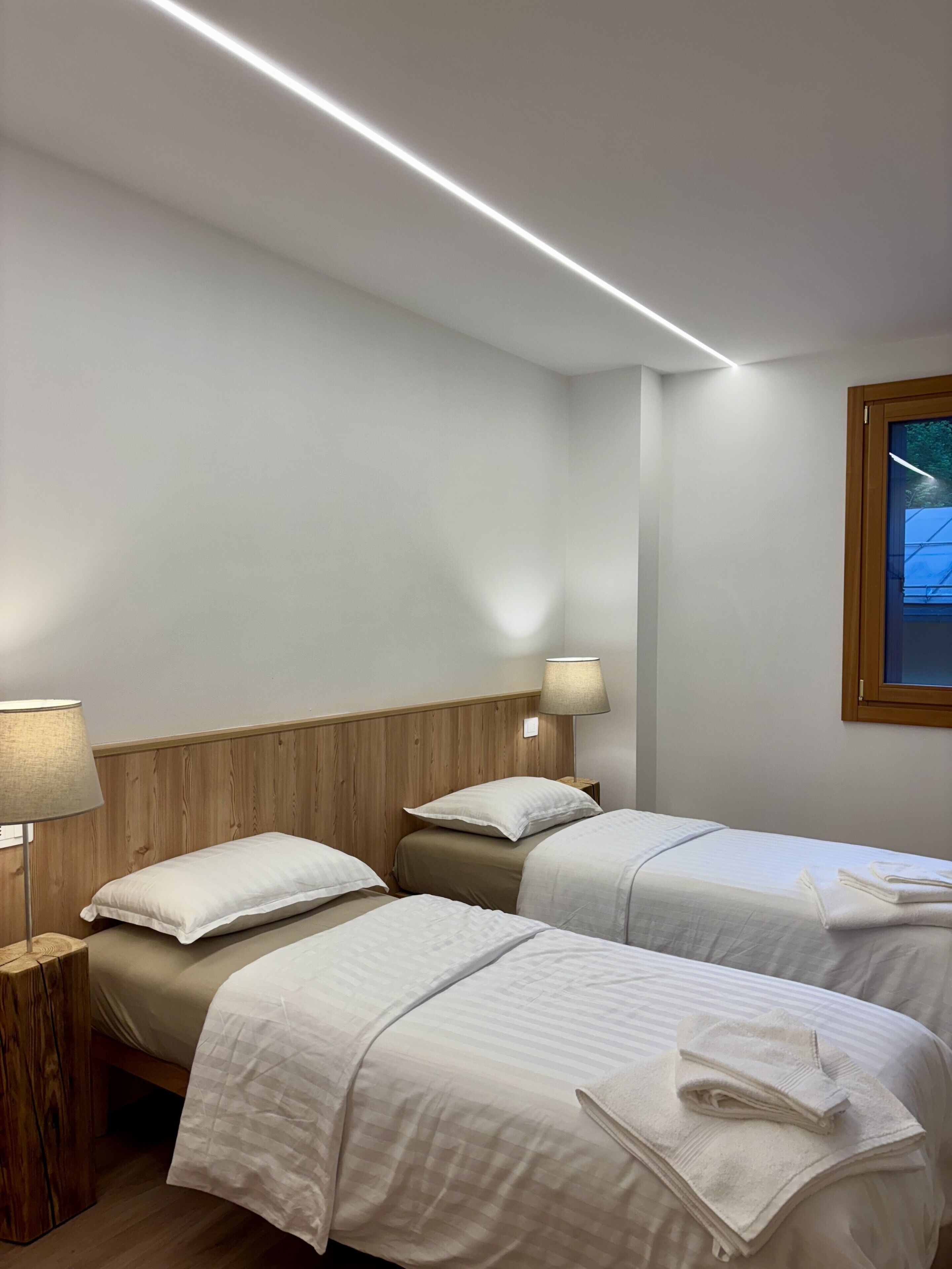 A hotel room with two beds, wooden headboards, bedside lamps, and a window with a view.