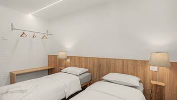 A hotel room with two beds, wooden headboards, bedside lamps, and a wall-mounted drying rack.