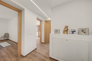 A hallway with wooden flooring, a grey chair, and a white wall with framed pictures. - Casa Baga – Apartment 5 with Mountain View and Balcony (Dont)