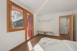 A bedroom with a large window, a bed, a bench, and a wall-mounted coat rack. - Casa Baga – Apartment 5 with Mountain View and Balcony (Dont)