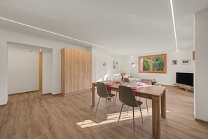 A modern dining area with a wooden table, chairs, and a TV in the background.