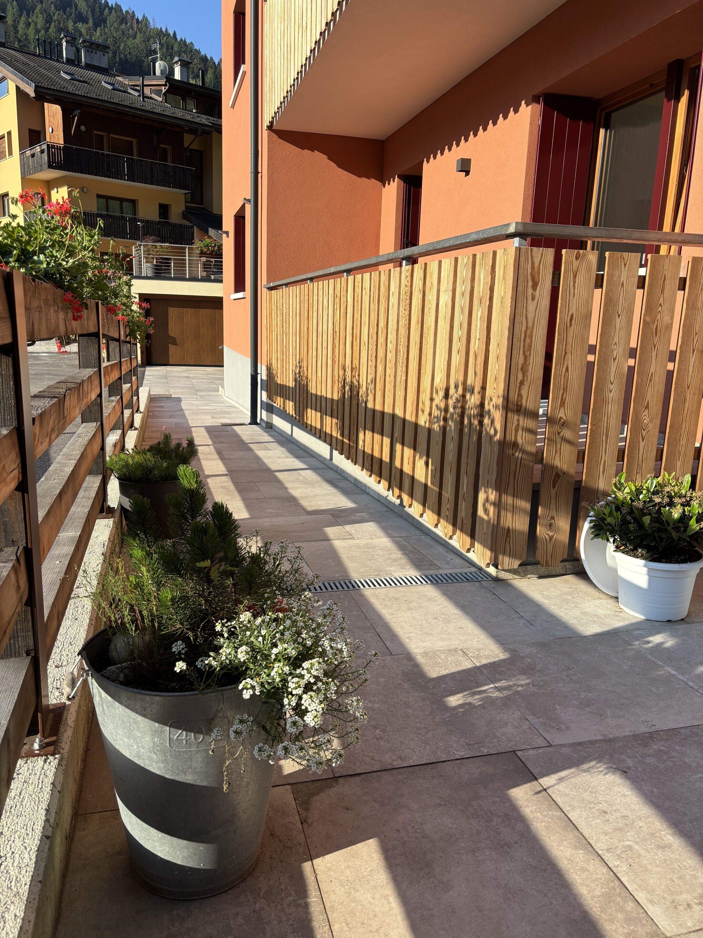 A courtyard with a wooden fence, potted plants, and a building with a balcony.