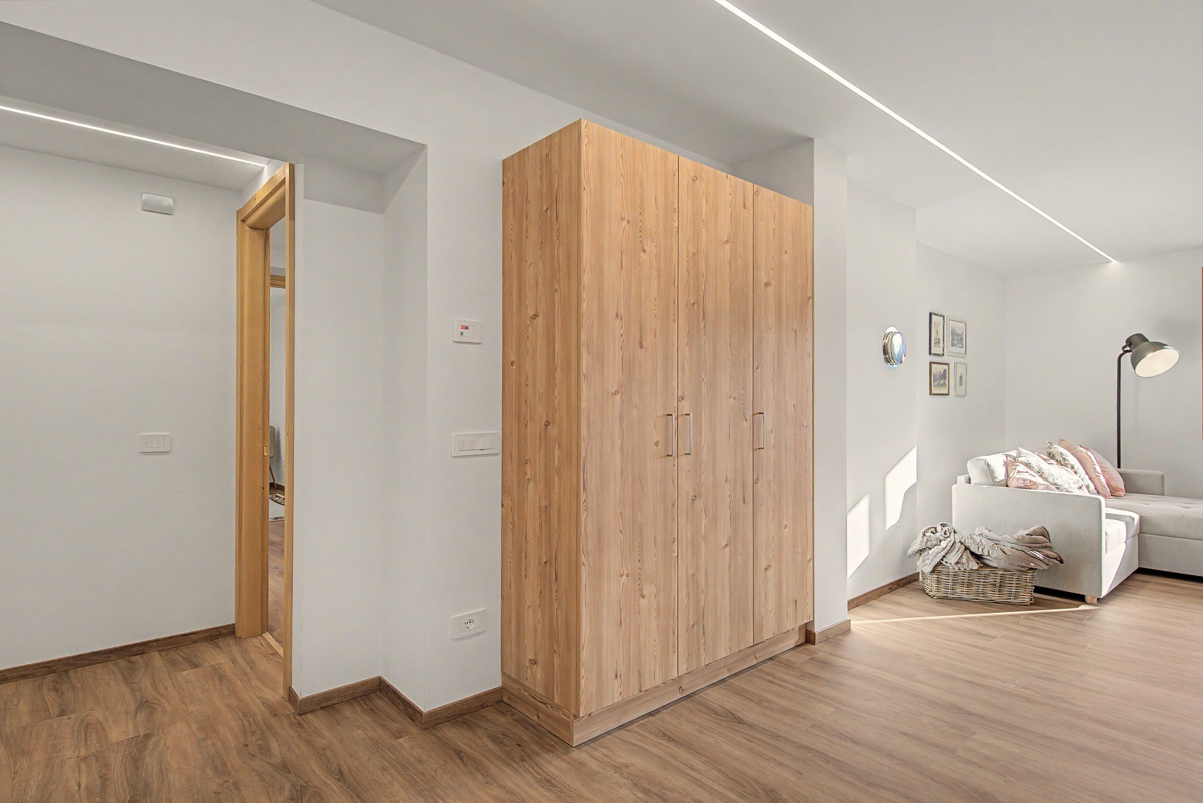 Una habitación moderna con un armario de madera, un sofá blanco y una lámpara de pie.
