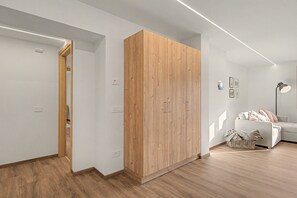 A modern room with a wooden wardrobe, a white sofa, and a floor lamp. - Casa Baga – Apartment 5 with Mountain View and Balcony (Dont)