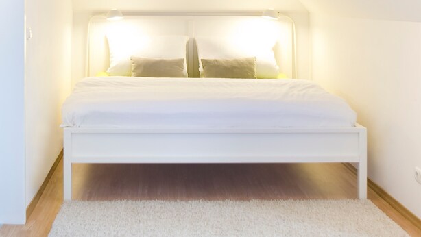 A white bed in a sloped ceiling room with a white carpet. - Stadt Land Fluss Studio Apartment '2' in Regensburg (Regensburg)