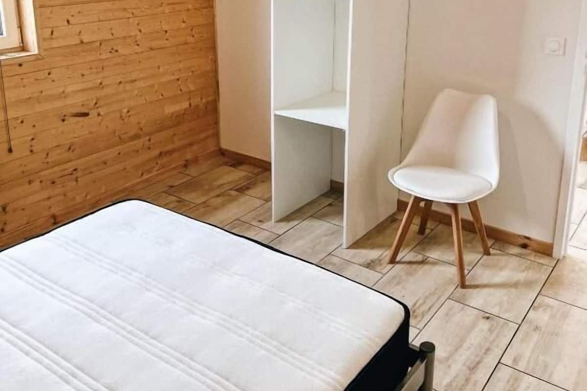 Een slaapkamer met een bed, een witte garderobe, een witte stoel en een houten wand.