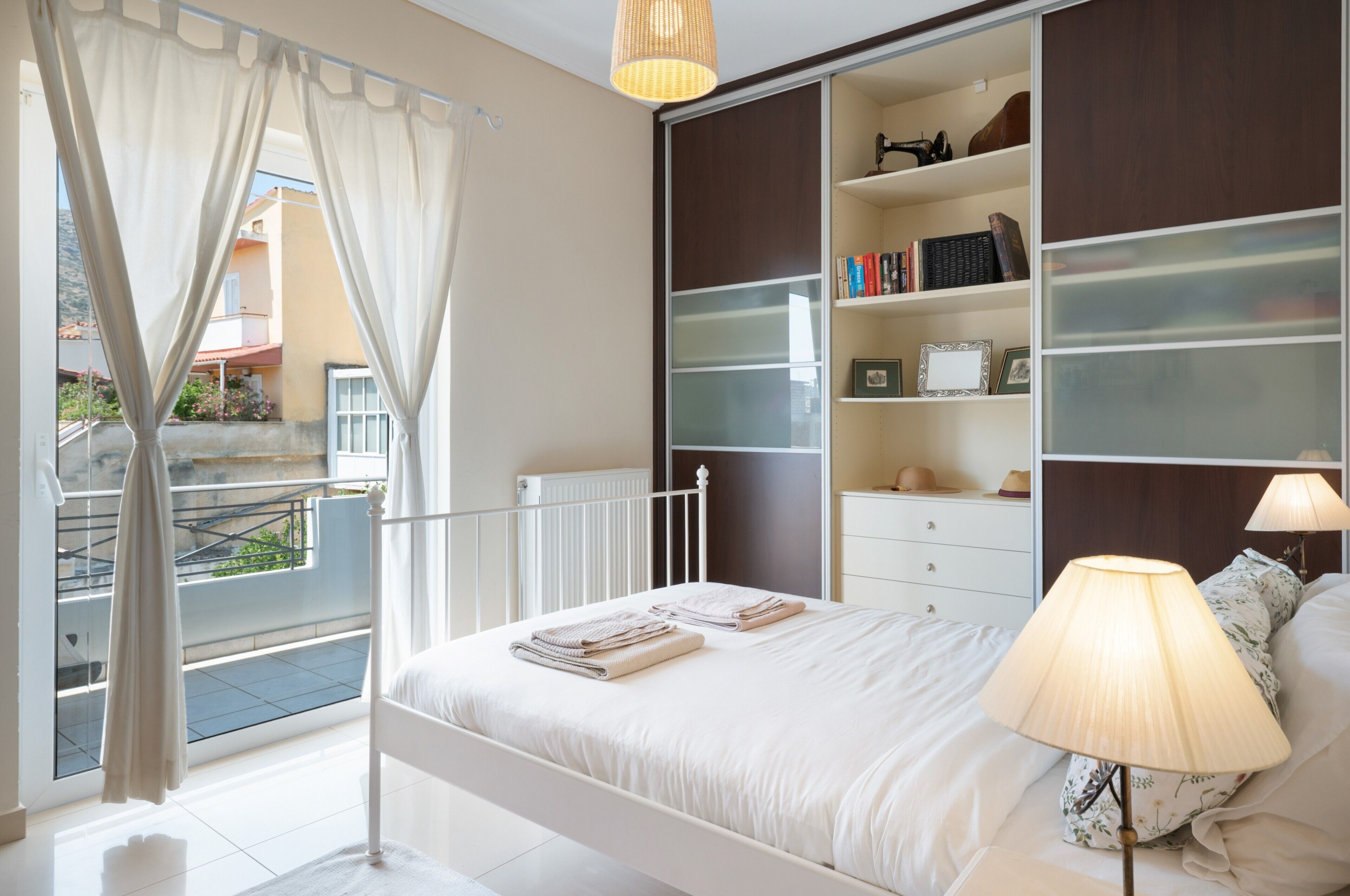 Un dormitorio con cama, lámpara de noche, armario y vistas al exterior.