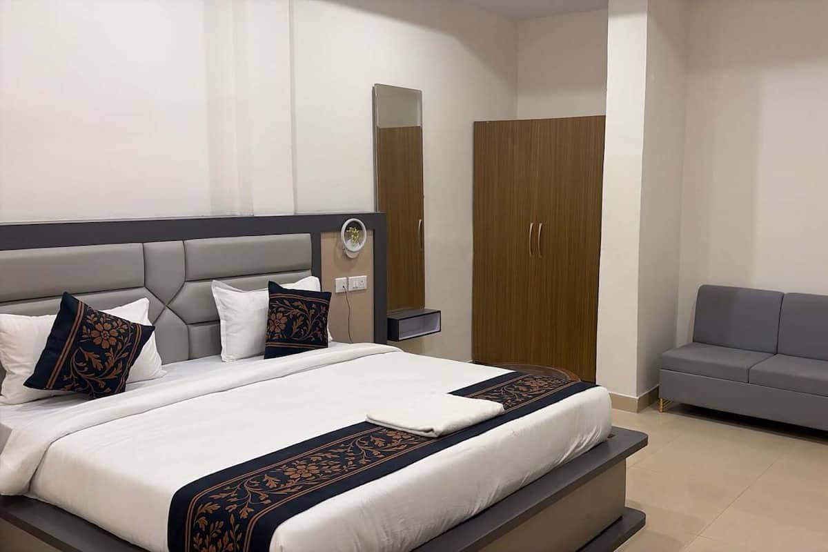 A modern hotel room with a large bed, a grey sofa, and a wardrobe.