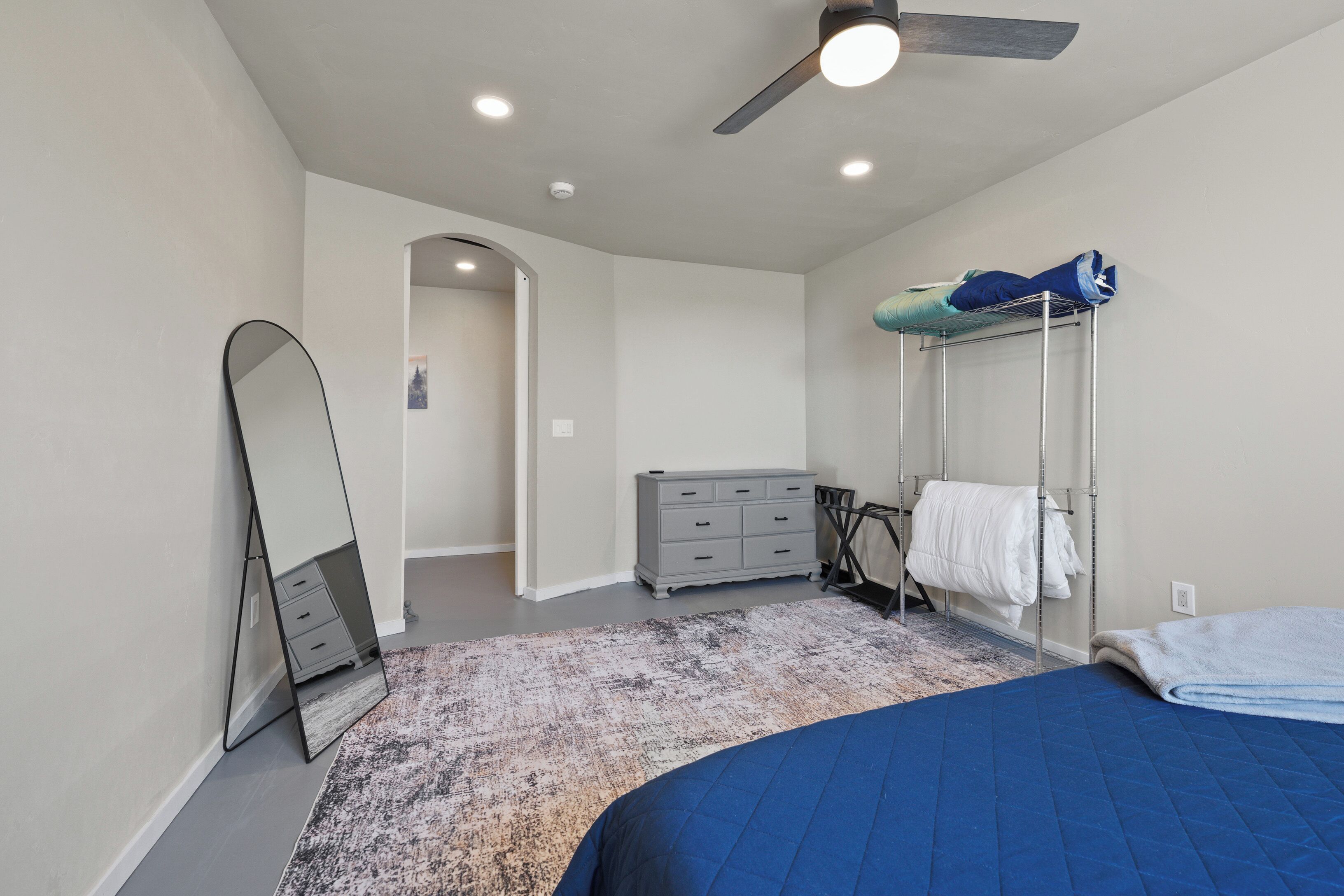 A bedroom with a bed, a dresser, a mirror, a ceiling fan, and a walk-in closet with hanging clothes.