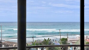 Vista de l'oceà a través d'una finestra, amb la platja i edificis al fons.