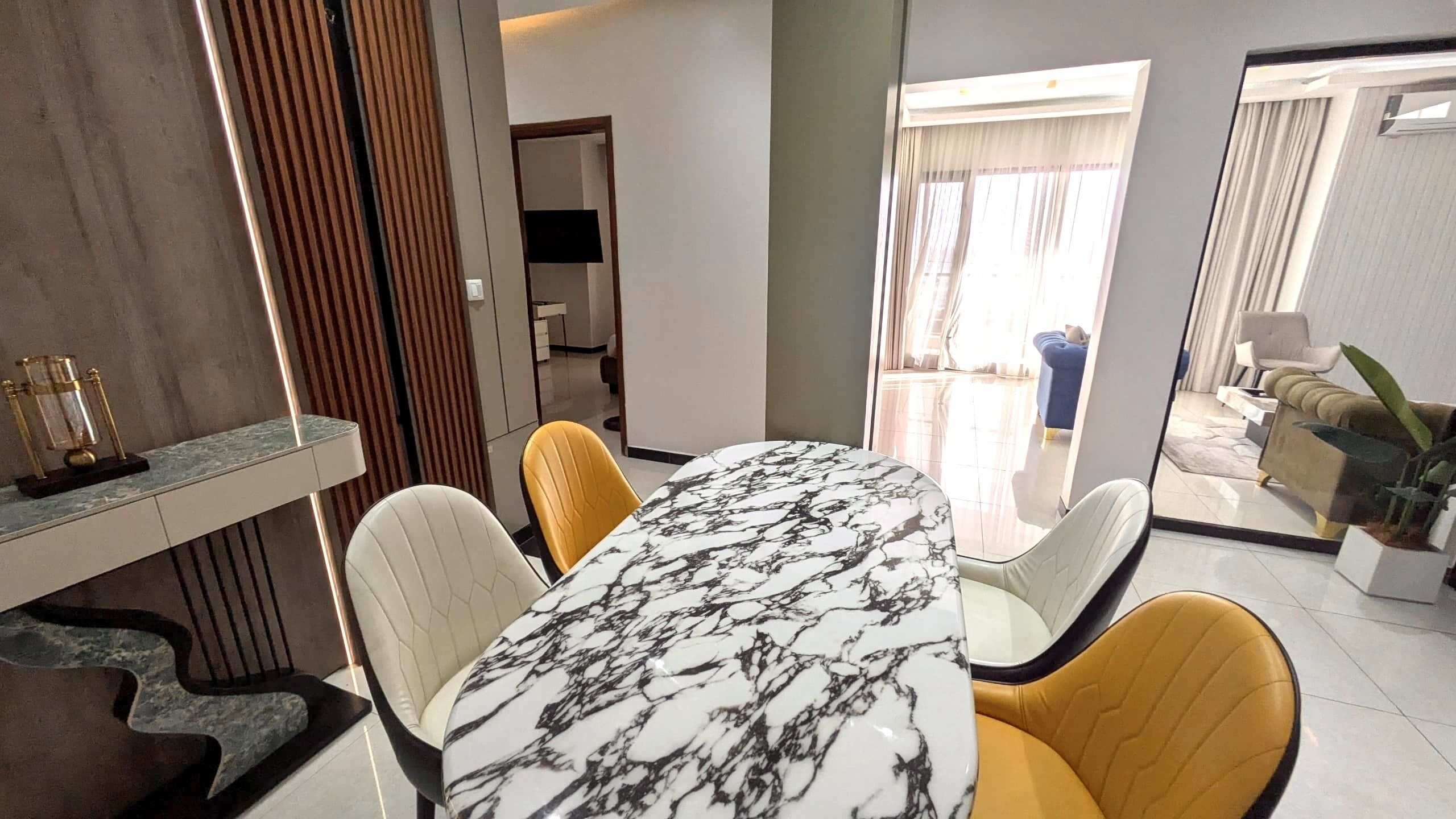 Zona pranzo con tavolo in marmo, due sedie gialle e un arredamento moderno.