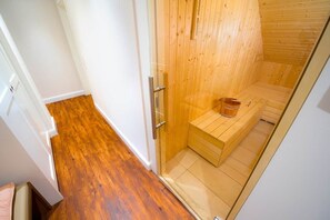 A sauna with a wooden bench, a glass door, and a wooden floor.