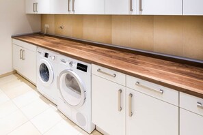 Ein moderner Waschraum mit Holztischplatte, zwei Waschmaschinen und weißen Schränken.