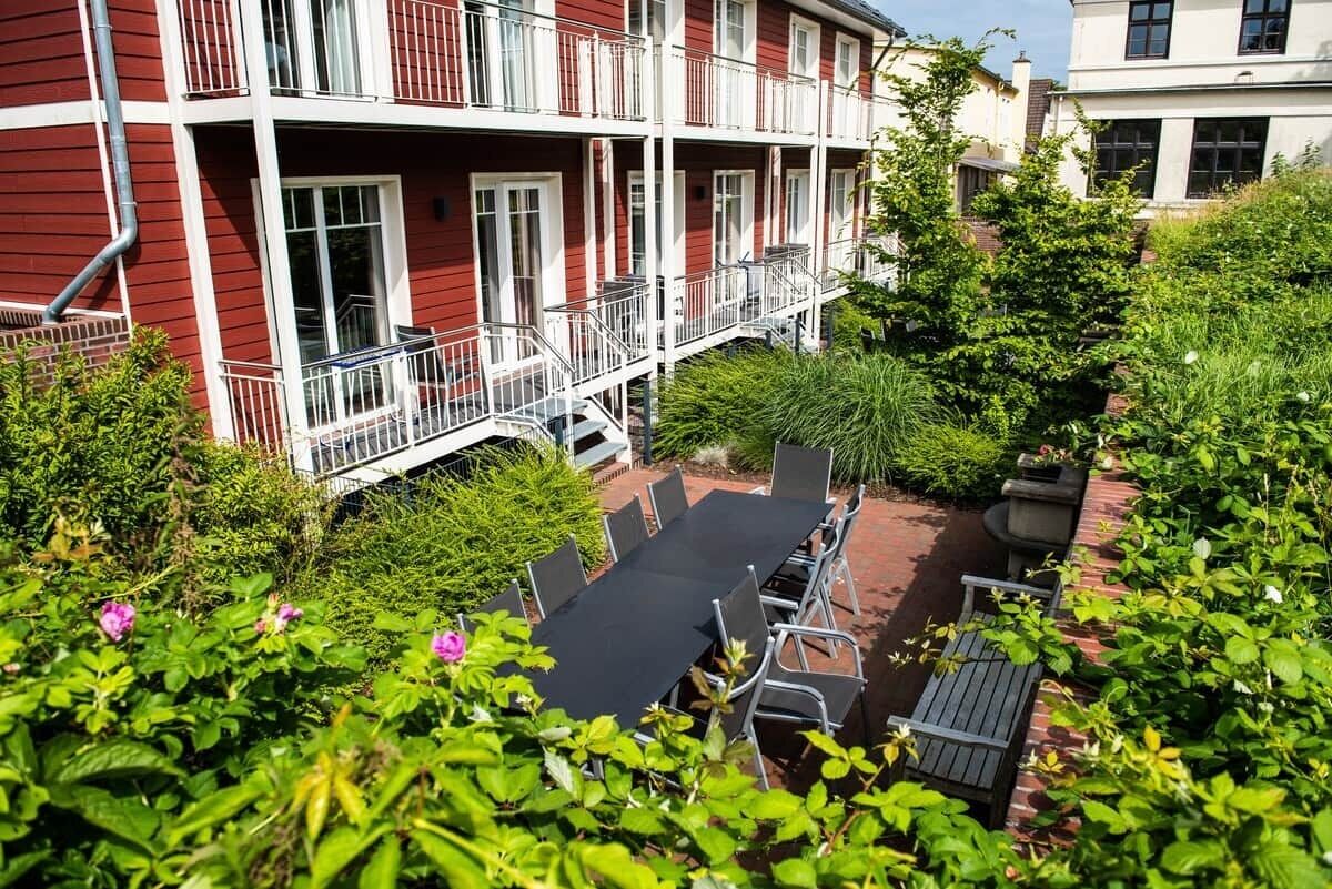A red building with balconies, a patio with chairs, and a garden area.