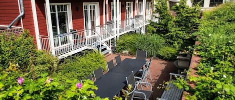A red building with balconies, a patio with chairs, and a garden area.