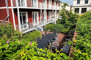 Ein rotes Gebäude mit Balkonen, einer Terrasse mit Sitzgelegenheiten und einem Garten.