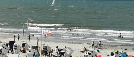 A beach with rows of beach chairs and umbrellas, a sailboat on the water, and people in the distance.