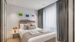 A modern bedroom with a bed, bedside tables, and a window with curtains. - Riverside Studio Manhattan Sleeps 2 - Chelsea AC (London)
