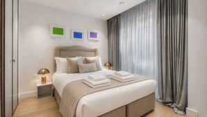 A modern bedroom with a large bed, bedside lamps, and a view of the outside through sheer curtains. - Riverside Studio Manhattan Sleeps 2 - Chelsea AC (London)