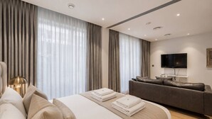 A modern hotel room with a large bed, a sofa, a flat-screen TV, and a large window with curtains. - Riverside Studio Manhattan Sleeps 2 - Chelsea AC (London)
