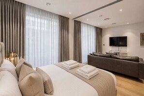 A modern hotel room with a large bed, a sofa, a flat-screen TV, and a large window with curtains. - Riverside Studio Manhattan Sleeps 2 - Chelsea AC (London)