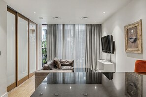 A modern living room with a sofa, a flat-screen TV, and a glass coffee table. - Riverside Studio Manhattan Sleeps 2 - Chelsea AC (London)