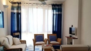 Ein Wohnzimmer mit einer Couch, zwei Sesseln, einem Couchtisch, einem Deckenventilator und einem Fernseher auf einem Schrank.