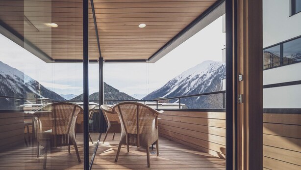 A balcony with wicker chairs, wooden flooring, and a view of snow-capped mountains. - Parsenn Resort Appartement/Fewo, Dusche, WC, 2 Schlafräume 3½-Zimmerwohnung by Interhome (Davos)