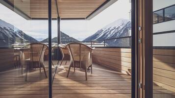 Un balcon avec des fauteuils en osier, un plancher en bois et une vue sur des montagnes enneigées.