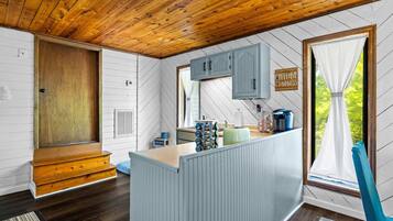 Ein Interieur einer Holzhütte mit Küchenzeile, Holzboden und einem Fenster mit Vorhängen.