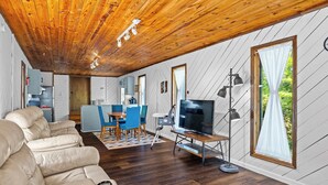 A cozy living room with a wooden ceiling, a sofa, a TV, and a dining area with chairs and a table.