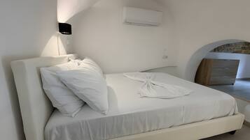 Un lit avec du linge de lit blanc, un climatiseur fixé au mur et une armoire en bois.