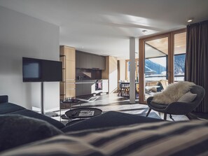Ein modernes Wohnzimmer mit Flachbildfernseher, einer Couch, einem Couchtisch und Blick auf eine Küche und einen Essbereich.