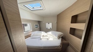 Interior compacto e bem iluminado, com cama, claraboia e compartimentos de armazenamento.