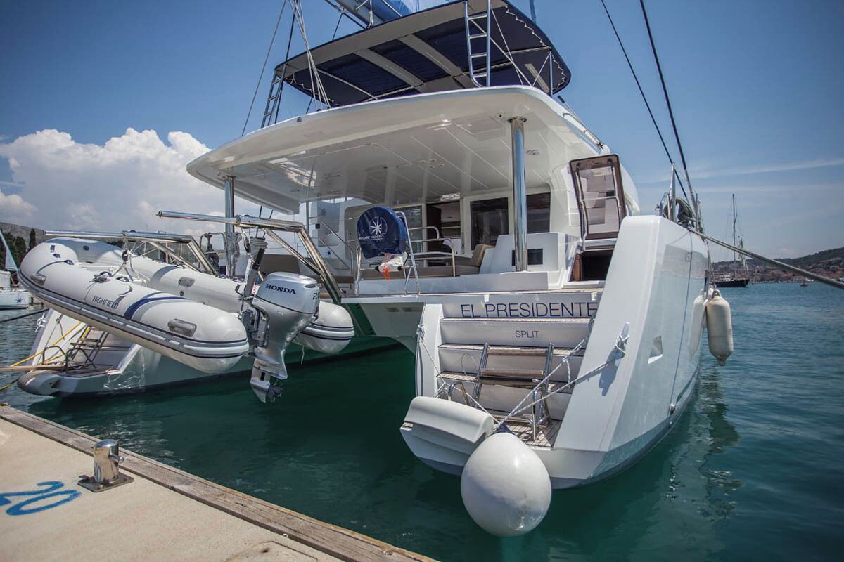 Un yacht était amarré dans une marina, avec une terrasse couverte, un espace aménagé pour s’asseoir et le nom « EL PRESIDENTE » clairement visible.