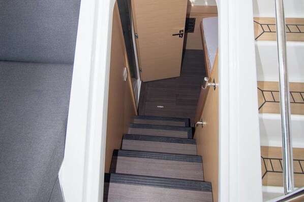 Una escalera de madera con barandilla metálica, que lleva a una habitación con una puerta y un ventanal pequeño.