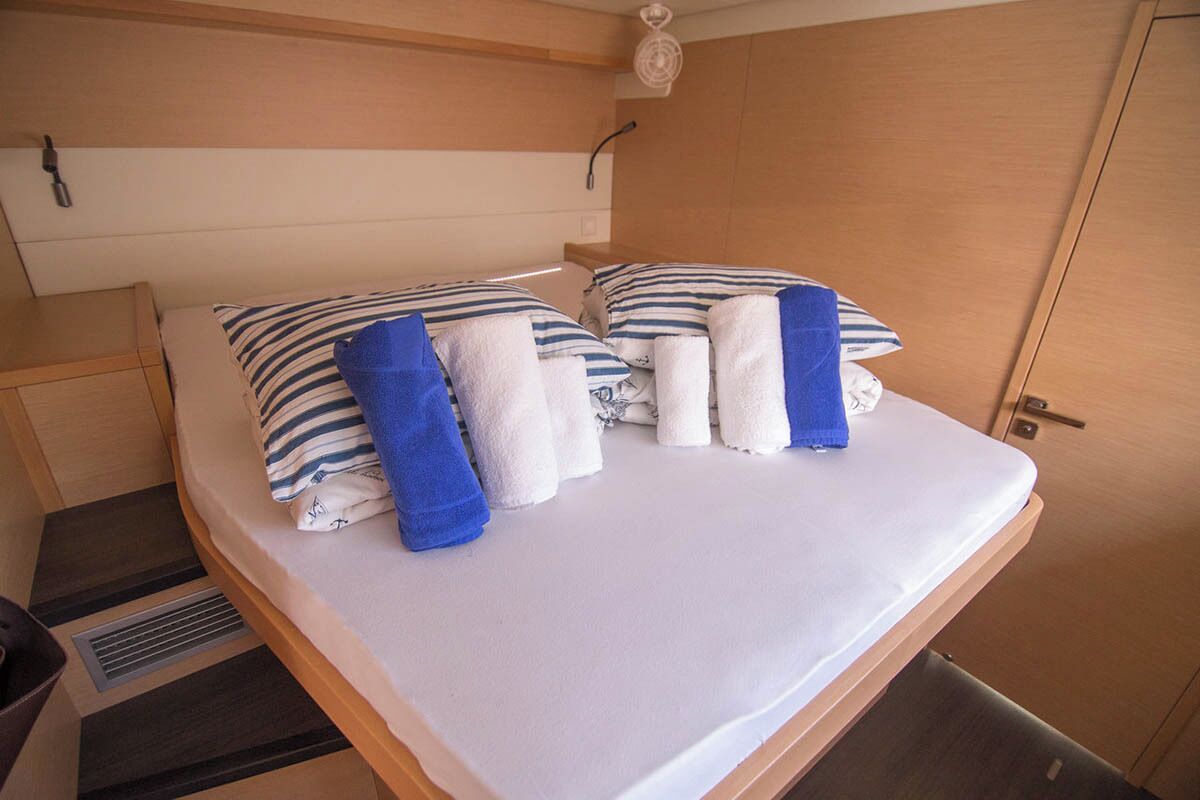 Een eenpersoonsbed met witte en blauw gestreepte kussens, een witte deken en twee opgerolde handdoeken.