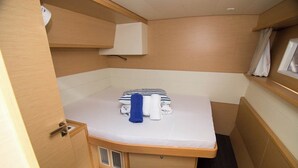 A compact cabin with a bed, a small storage cabinet, a window with curtains, and a built-in shelf.