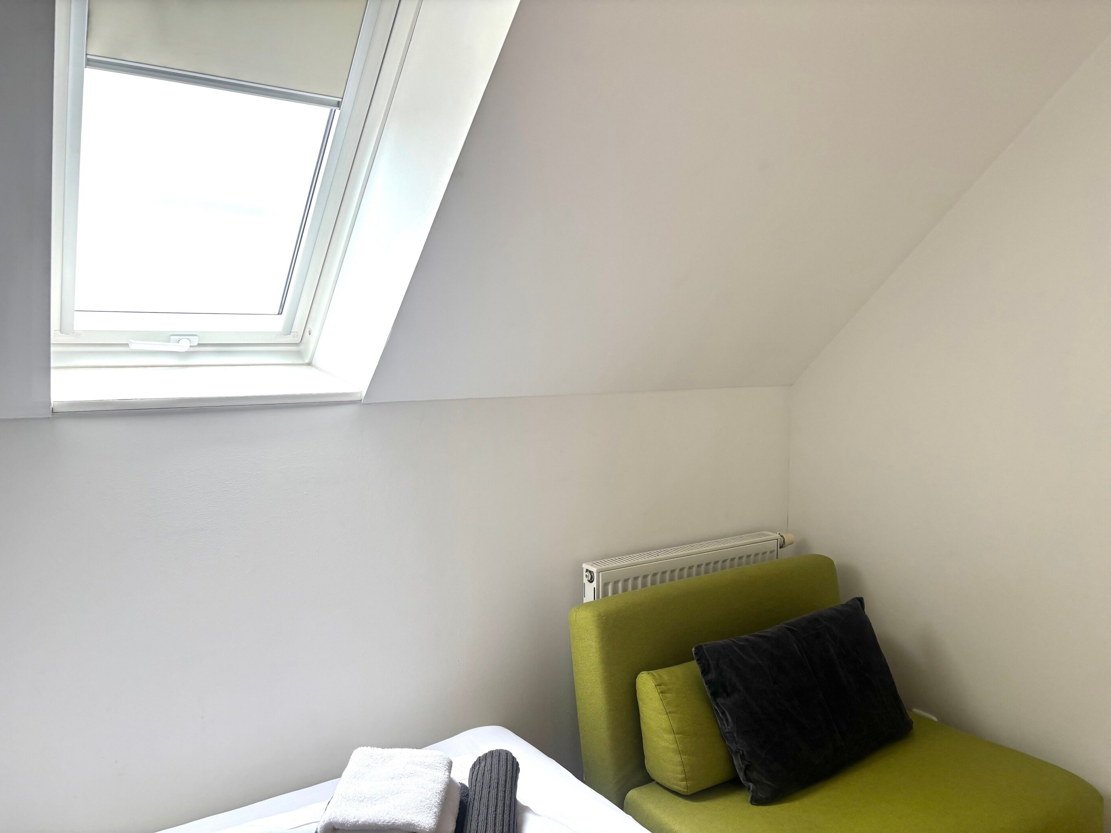 A room with a skylight, a radiator, a green sofa with cushions, and a white bed.