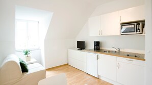 Eine moderne Küche mit weißen Schränken, einer Mikrowelle, einer Kaffeemaschine und einer kleinen Pflanze auf einem Fensterbrett.
