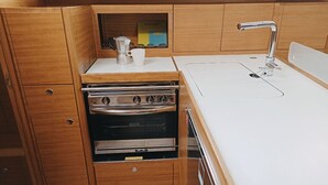 A compact kitchen with wooden cabinetry, a built-in oven, and a white countertop. - Sun-Kissed Sailing Adventure in Istria, Croatia (Pula)