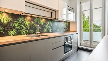 Una cocina moderna con un ventanal grande, horno empotrado y salpicadero con diseño de hojas tropicales.
