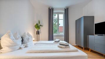 A hotel room with a large bed, a television, a wardrobe, and a window with curtains.