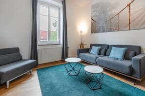 A modern living room with a grey sofa, two white round tables, and a blue rug.