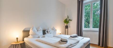 Une chambre d’hôtel avec un lit, une table de chevet, une plante en pot et une fenêtre avec des rideaux.