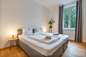 A hotel room with a bed, a bedside table, a potted plant, and a window with curtains.